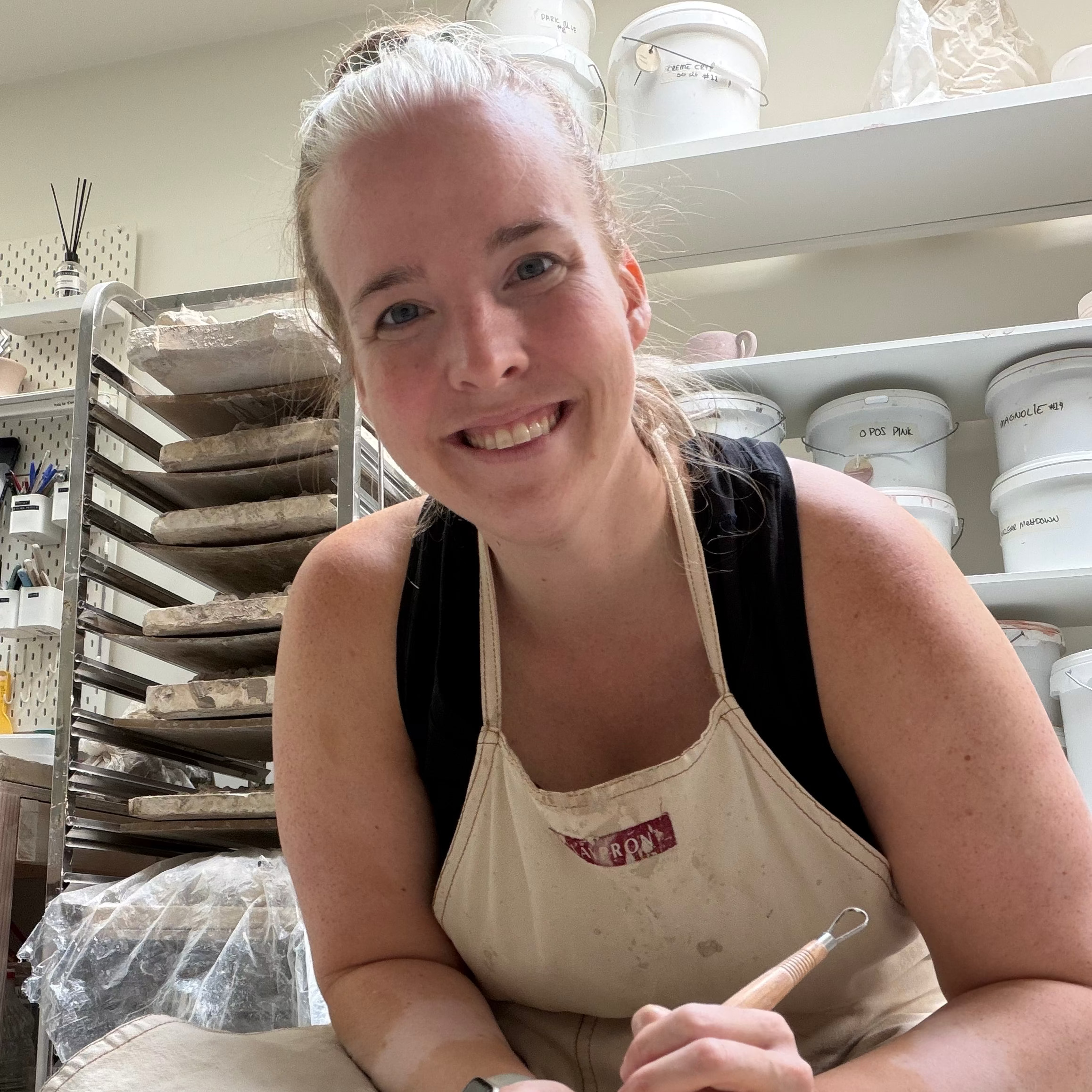 Keri Byrne sitting at a pottery wheel, trimming a small dish
